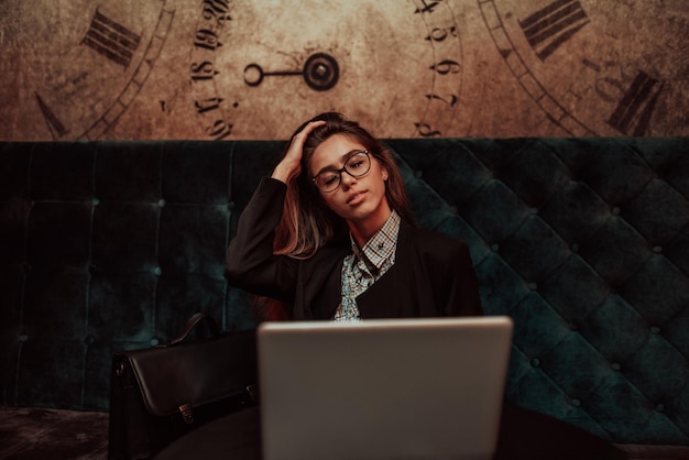 Cansado jovem estudante estudando on-line enquanto está sentado com laptop e notebook no refeitório feminino freelancer descansando o rosto por lado com falta de expressão facial olha para o lado Foco seletivo