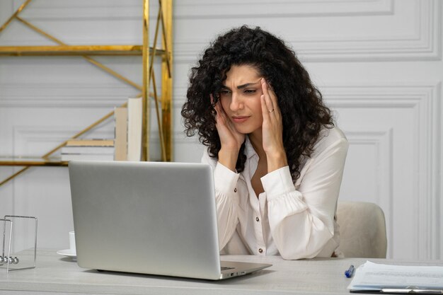 Cansado joven indio curlyhaired sufre de migrañas sobrecargado de trabajo en un portátil un