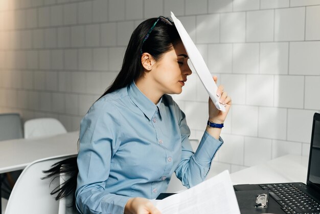 Cansado joven morena con camisa azul trabajando duro en la computadora portátil