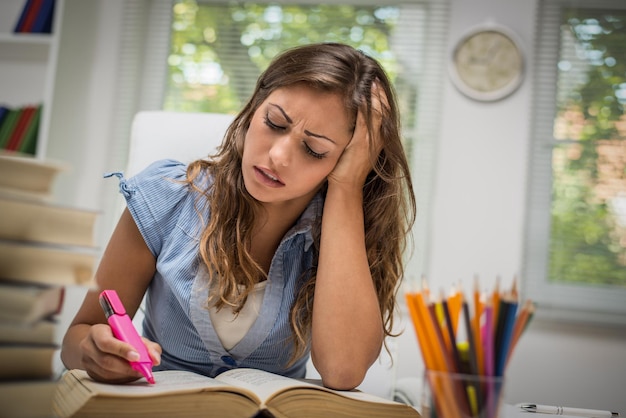 Cansado linda adolescente com muitos livros aprendendo na biblioteca.