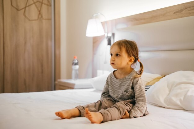 Cansado niño triste niño niña sentada en la cama en la habitación del hotel