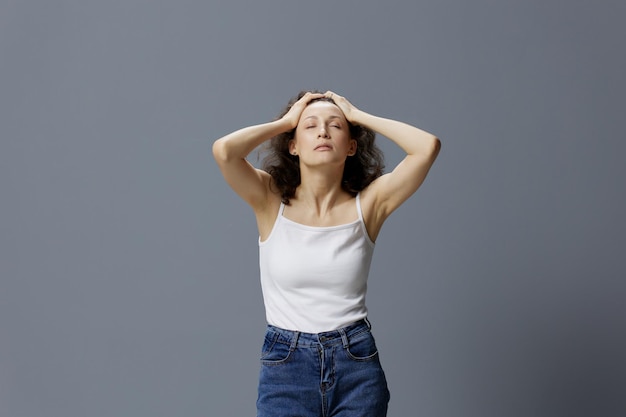 Cansado relaxante calma encaracolada mulher bonita em camiseta branca básica gosta de massagem na cabeça fechando os olhos posando isolado sobre fundo azul cinza Pessoas Estilo de vida Emoções conceito Espaço para texto