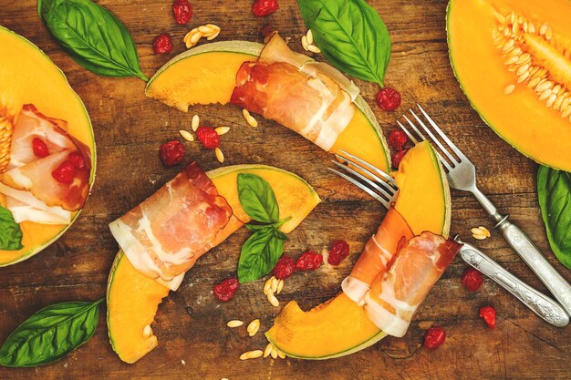 Cantaloupe-Melone in Scheiben geschnitten mit Prosciutto-Jamon-Basilikumblättern, Feige und getrockneter Kirsche, italienische Vorspeise auf Holzhintergrund