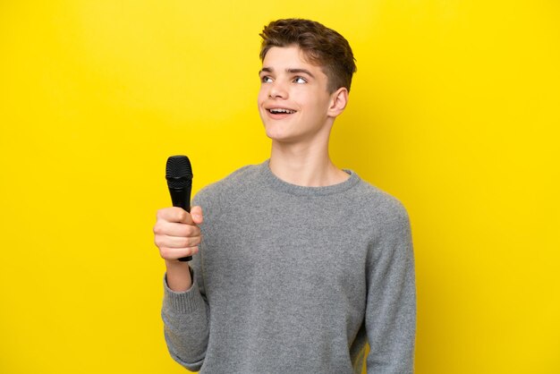 Cantante Adolescente hombre recogiendo un micrófono aislado sobre fondo amarillo mirando hacia arriba mientras sonríe