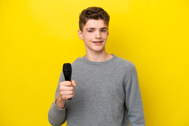 Cantante Adolescente hombre recogiendo un micrófono aislado sobre fondo amarillo sonriendo mucho