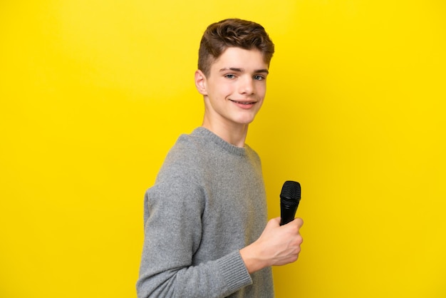 Cantante Adolescente hombre recogiendo un micrófono aislado sobre fondo amarillo sonriendo mucho