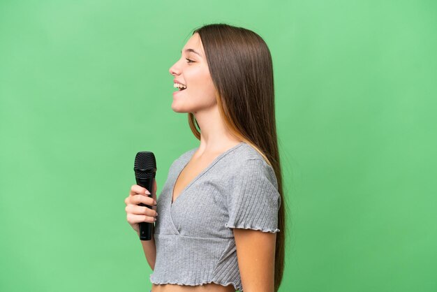 Cantante adolescente recogiendo un micrófono sobre un fondo aislado riéndose en posición lateral