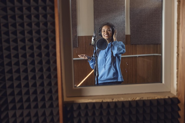 Cantante africana adolescente con auriculares canta en el micrófono trabajando en un estudio de voz con