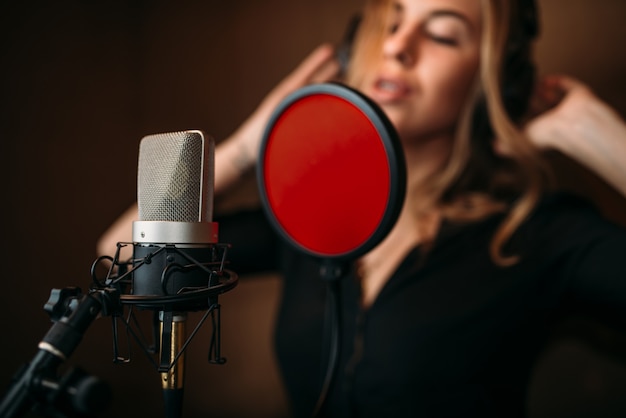 Cantante en auriculares contra micrófono, grabación de canciones en estudio de música.