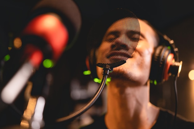 Cantante con auriculares trabajando para grabar y tocar una voz musical con un micrófono profesional en un estudio de audio. El vocalista canta una canción con un músico e ingeniero de sonido con transmisión en vivo.