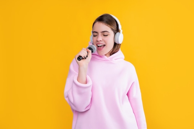 Cantante joven feliz en auriculares con micrófono sobre fondo amarillo