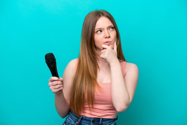 Cantante mujer caucásica recogiendo un micrófono aislado sobre fondo azul con dudas