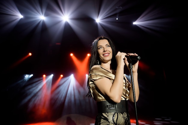 Cantante con un vestido en el escenario bajo los rayos de luz brillante con humo.