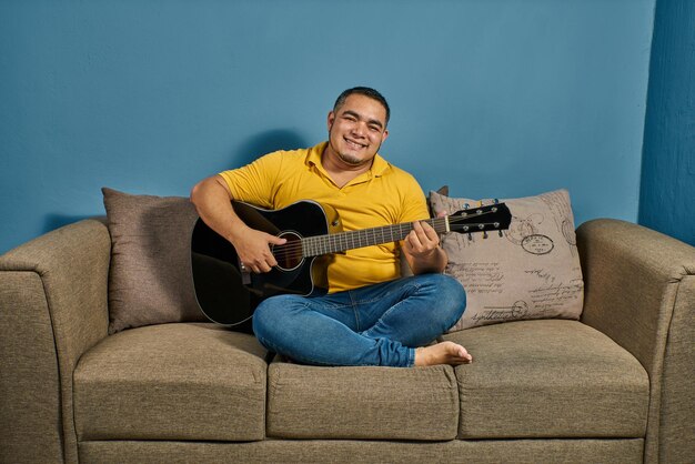 Cantar y tocar la guitarra en casa en un sofá relajado