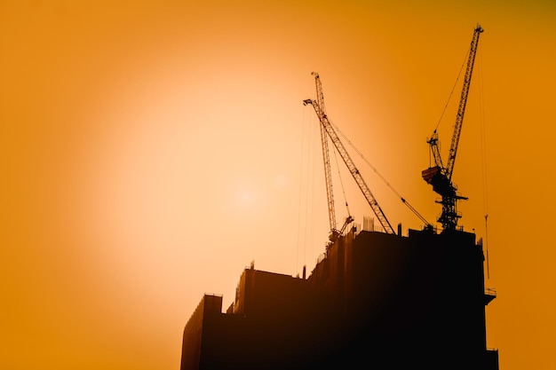 Canteiro de obras com guindastes em fundo por do sol.