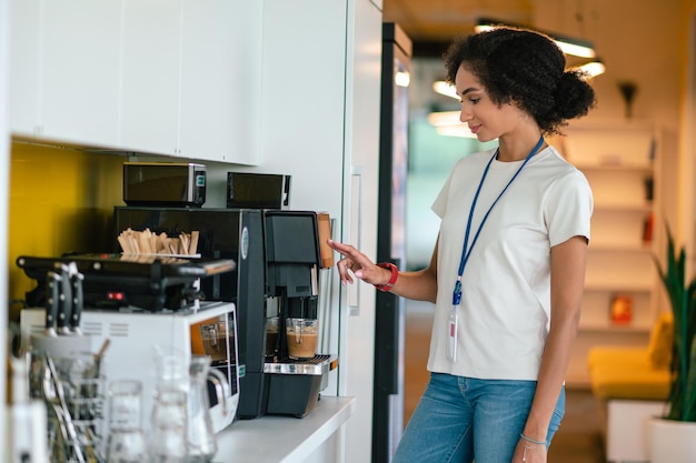 En la cantina. Mujer joven de cabello oscuro en la oficina haciendo café en la cantina de la oficina