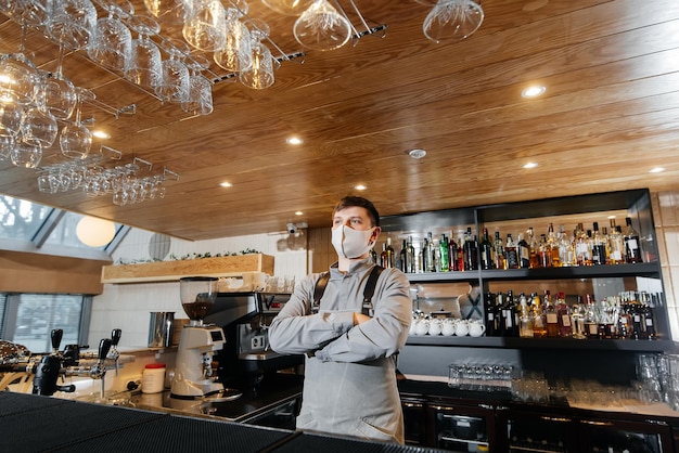 Un cantinero elegante con una máscara y un uniforme se encuentra cerca del bar durante la pandemia El trabajo de los restaurantes y cafés durante la pandemia