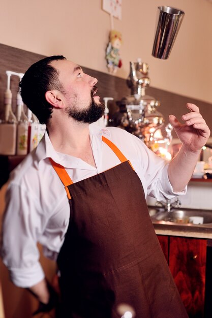 El cantinero o barista hace malabares con una coctelera de metal. Espectáculo de bartender