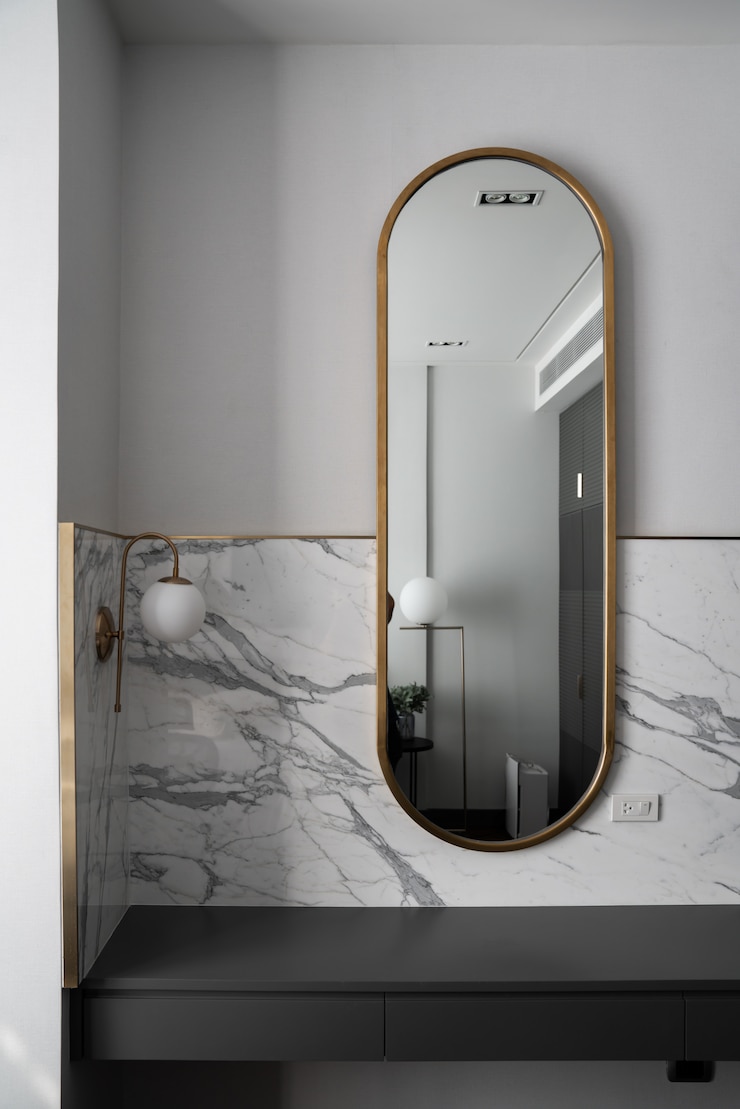 Foto canto de trabalho do quarto com composição de espelho de ouro inoxidável com parede de mármore branco e luminária de parede de ouro