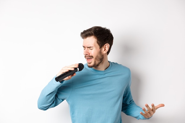 Cantor realizando música em fundo branco. Jovem cantando no microfone no karaokê