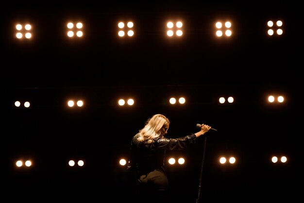 Cantora em cena no clube. Iluminação de palco brilhante.