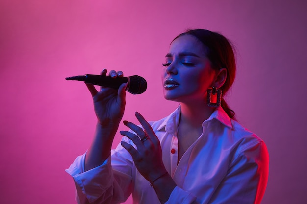 Cantora em luz de néon. Menina de camisa branca com microfone. Conceito de arte, emoções humanas, música.