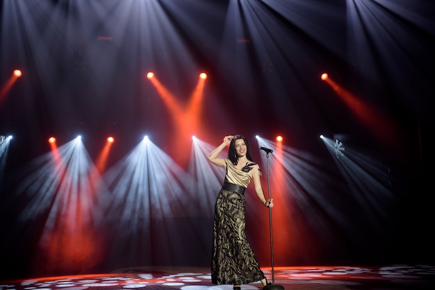 Cantora em um vestido no palco sob os raios de luz brilhante com fumaça.