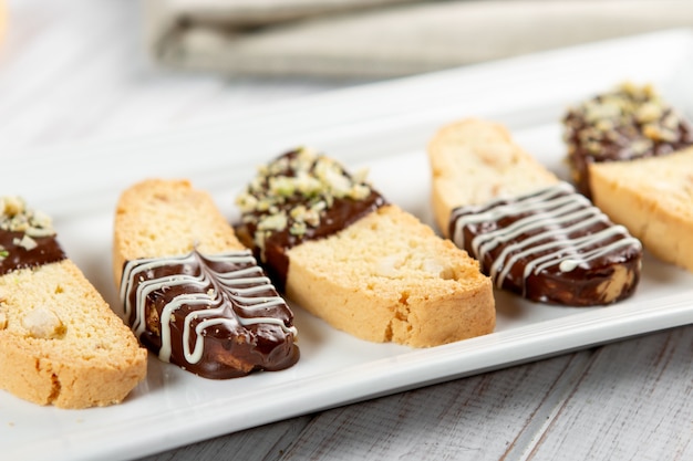 Cantuccini-Kekse. Italienisches Biscottiplätzchen auf weißer Platte auf einem weißen hölzernen Hintergrund. Ansicht von oben