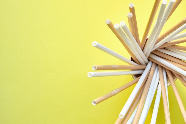 Canudos de papelão marrom e branco colocados em espiral dentro de um vidro de papelão no lado direito da imagem em um fundo amarelo