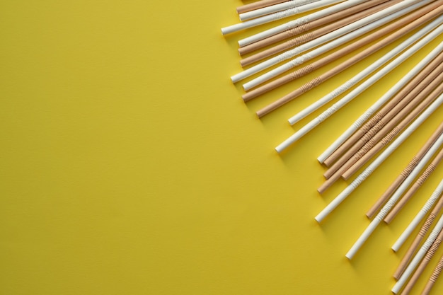 Canudos de papelão marrom e branco colocados em uma linha no canto superior direito da imagem em um fundo amarelo