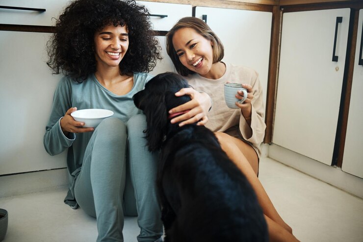 Foto cão de amigos e manhã feliz na cozinha de casa ou mulheres com bebida de café e tomando café da manhã no chão do apartamento casal animal ou animal de estimação em casa com amor, cuidado e apoio de meninas