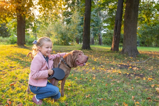 Cão de shar pei do puro-sangue com a menina pequena no parque. Shar-pei está olhando de lado.