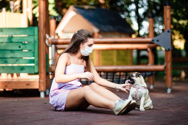 Cão feliz Uma garota com uma máscara segura um cachorro nos braços Jovem mulher andando com um cachorro pug no parque de verão Retrato de um pug Retrato de um lindo cachorrinho pug O cachorro está deitado no chão