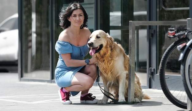 Cão retriever dourado na coleira e menina bonita sentada na rua perto do supermercado cachorro de estimação de raça pura