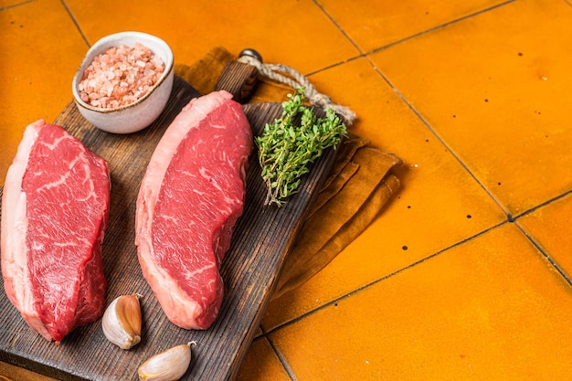 Cap Rump Steak bife de carne bovina crua com tomilho e sal em tábua de madeira de açougueiro Fundo laranja Vista superior Espaço de cópia