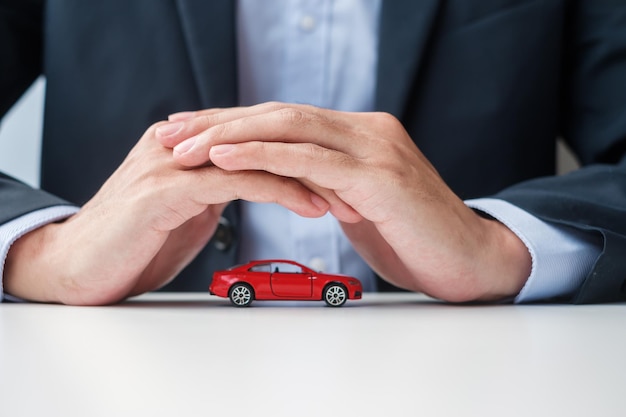 Foto capa de mão de empresário ou brinquedo de carro vermelho de proteção na mesa reparo de garantia de seguro de carro conceito bancário e dinheiro financeiro