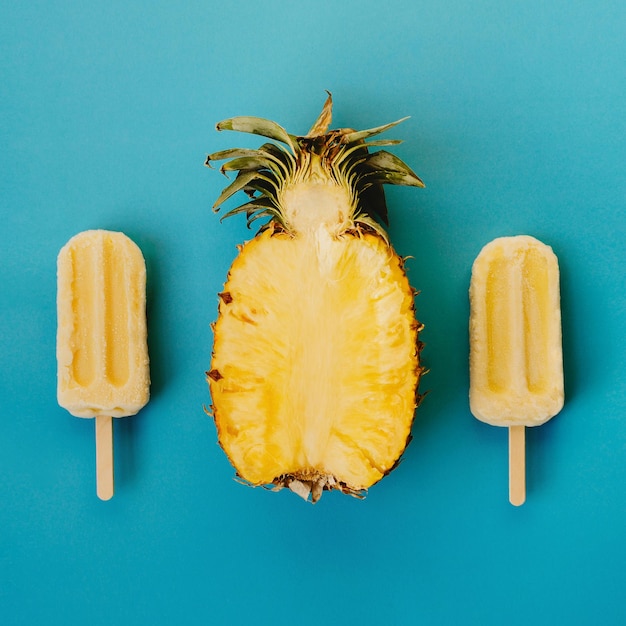 Foto una capa plana tropical de tres paletas veganas y la mitad de piña madura sobre un fondo cian