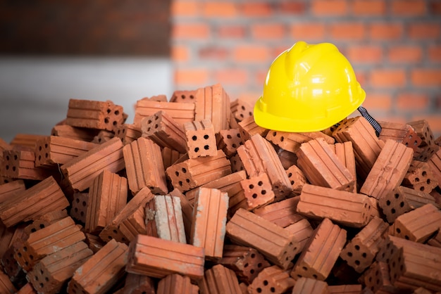 Foto capacete amarelo colocado sobre uma pilha de tijolos ou tijolos feitos de barro laranja. o material de construção de base é o canteiro de obras.