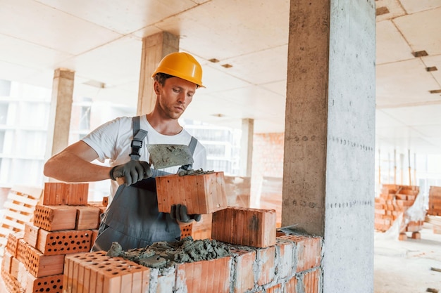 Foto capacete de cor amarela jovem trabalhando de uniforme na construção durante o dia