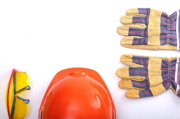 Capacete de segurança alaranjado, luvas de couro do trabalho e óculos de segurança em um fundo branco. Copie o espaço.