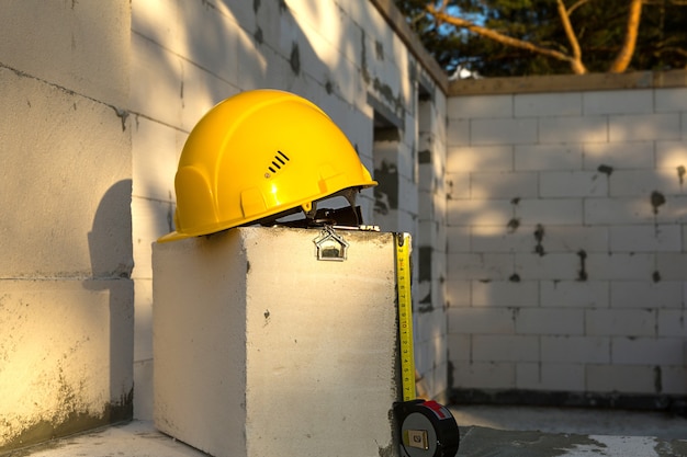 Capacete de segurança amarelo de construção, chave e uma fita métrica para abrigar na janela de um alojamento feito de blocos de concreto poroso. Construção chave na mão, futura casa, engenharia, construção. Segurança do trabalho. Copie o espaço