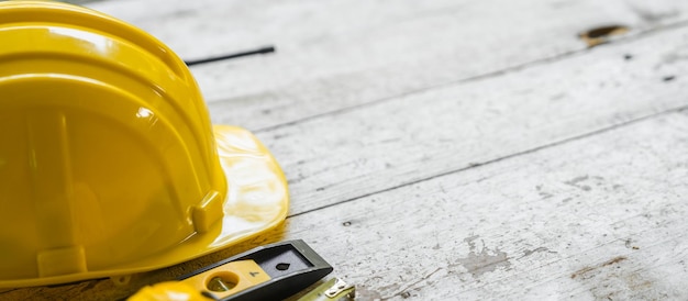 Foto capacete de segurança amarelo e desenhos arquitetônicos enrolados em uma mesa de madeira