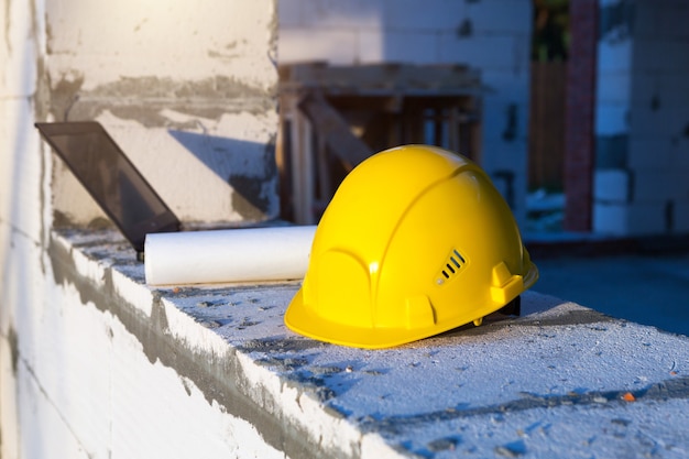 Capacete de segurança de construção, desenho e laptop na janela de uma casa em construção. fluxo de trabalho, arquitetura e engenharia.