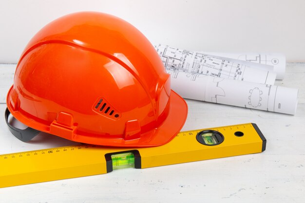 Capacete de segurança, desenhos em papel, blueprits e nível de construção em uma mesa branca. O trabalho de um engenheiro civil.