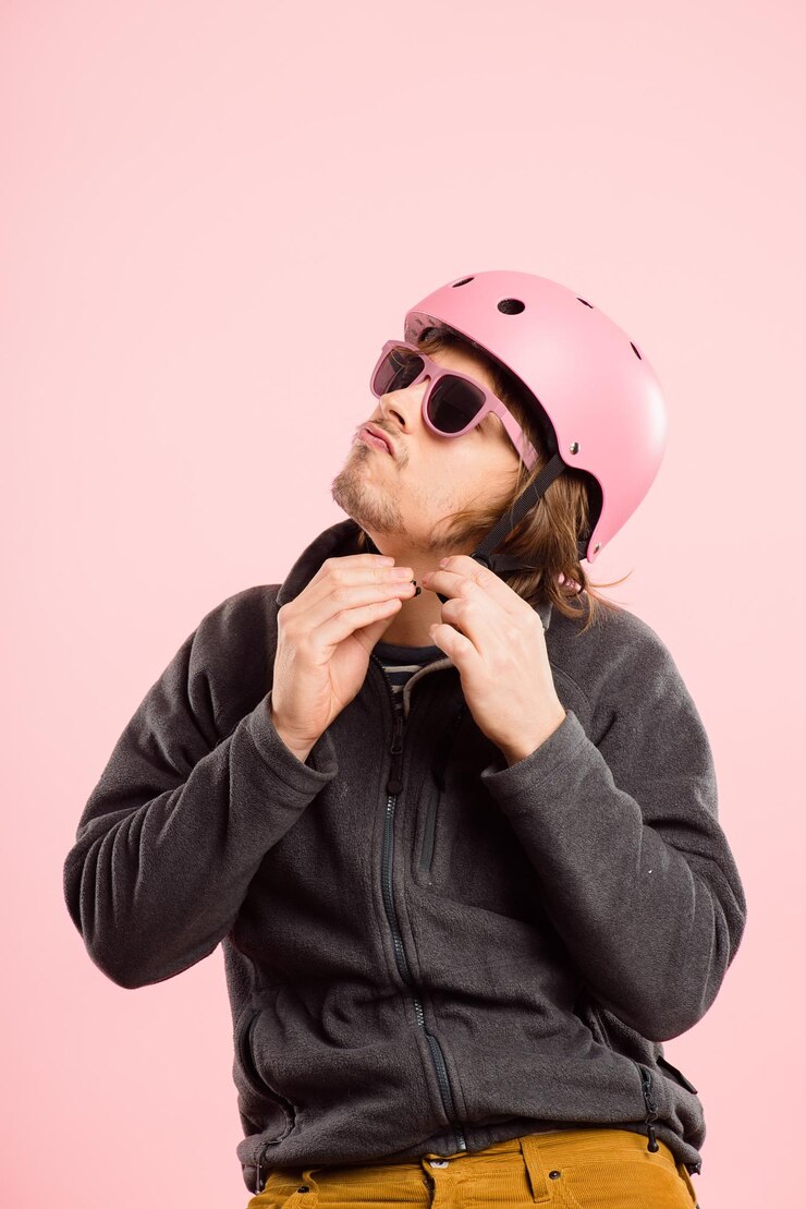 Foto capacete de segurança e óculos de sol com o homem no estúdio isolado em fundo rosa para ciclismo óculos se preparando e prendendo com a pessoa no espaço simulado para treinamento de cardio, moda ou fitness
