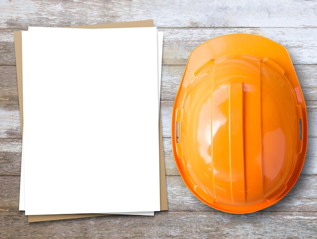 Capacete de segurança laranja e papel branco no fundo da mesa de madeira