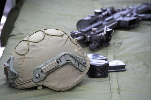 Capacete militar ao lado do rifle com mira em uma superfície de tecido e revistas visíveis na configuração