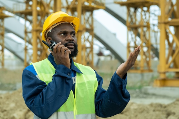 Capataz africano em trajes de trabalho falando no walkie-talkie no canteiro de obras