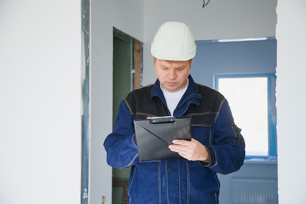 Capataz do construtor com um capacete branco em uma construção dentro de casa, conceito de reforma plana, capataz profissional no trabalho