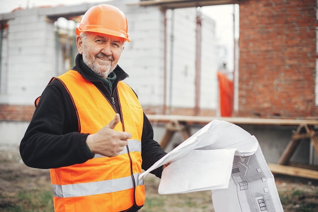 Foto capataz masculino senior en casco que aprueba la construcción de una nueva casa moderna de acuerdo con los planos